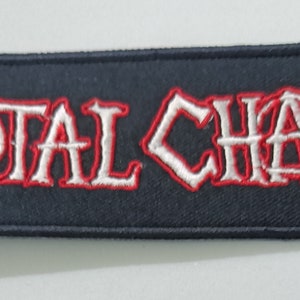 Pode incluir: Um patch retangular preto com as palavras "TOTAL CHAOS" bordadas em branco com uma contorno vermelho. O patch é retangular com uma borda preta.