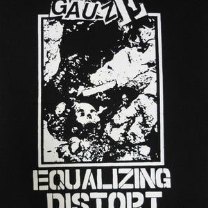 May include: Black graphic tee with a white design. The design features the word "GAUZ" above a rectangular image of a skull and rock formation. Below the image, the words "EQUALIZING DISTORT" are printed in a stencil font.
