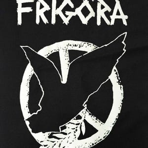 May include: Black graphic featuring the word "FRIG&Ouml;RA" in white, stylized, distressed lettering above a white peace symbol. Inside the peace symbol is a white dove with outstretched wings and an olive branch.