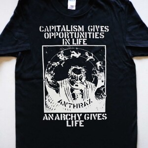 Puede incluir: Camiseta negra con texto blanco que dice "El capitalismo da oportunidades en la vida" y "La anarquía da vida". La camiseta presenta una imagen en blanco y negro de un hombre con barba y bigote.