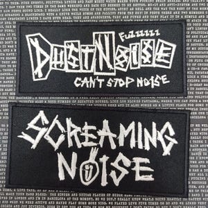 Puede incluir: Dos parches bordados en blanco y negro con los nombres de las bandas "Dust Noise" y "Screaming Noise". El parche "Dust Noise" tiene el texto "Can't Stop Noise" debajo del nombre de la banda. El parche "Screaming Noise" tiene una imagen estilizada de un micrófono.