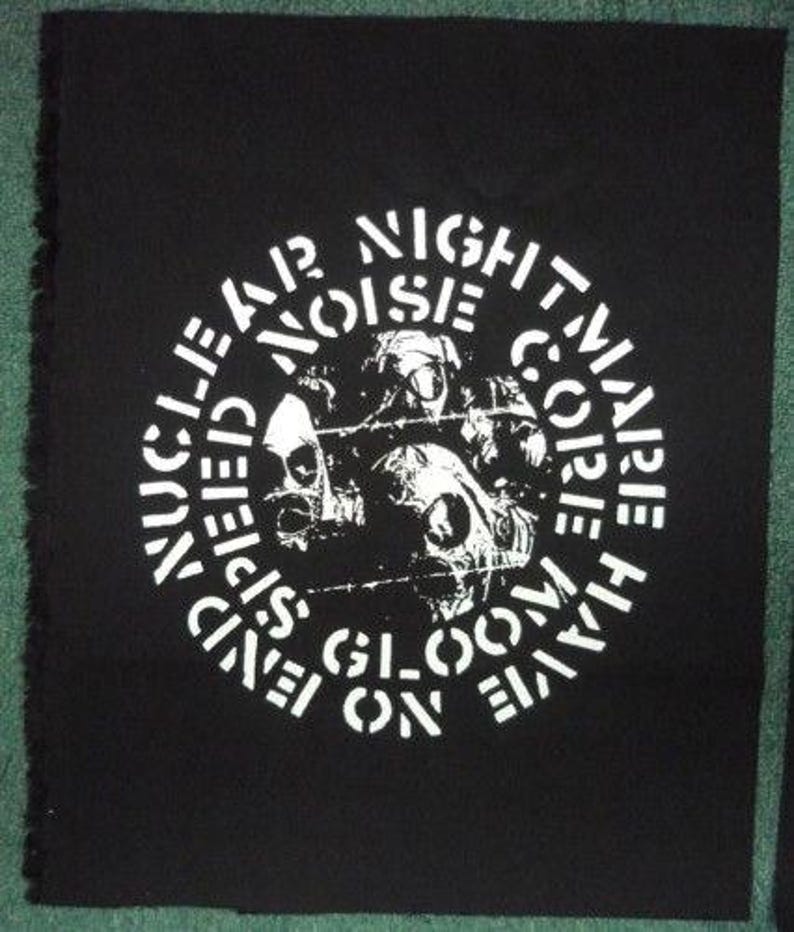 May include: Black square patch with white text and a skull graphic. The text reads "NUCLEAR NOISE NIGHTMARE CORE HAVE SEEN BLOOM ON FLAME". The patch has a raw edge.