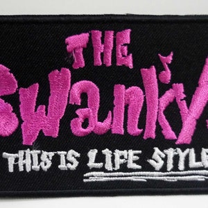 May include: Black embroidered patch with pink lettering that reads "The Swanky's This Is Life Style".