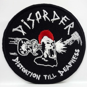 May include: A black and white embroidered patch with the text "Disorder" in a stylized font. The patch features a white silhouette of a person with a red mohawk, holding a guitar and a microphone. The text "Distortion Till A Deafness" is written in a circle around the image.