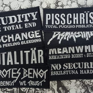 Puede incluir: Una colección de parches rectangulares de tela negra con texto bordado en blanco. Los parches muestran nombres de bandas y frases como CRUDITY THE TOTAL END, DISCHANGE SEEING FEELING BLEEDING, TUTALITÄR, PROTES BENGT IN BENGT WE TRUST, PISSCHRIST TOTAL FUCKING PISSLICKERS, MEANWHILE REMAINING RIGHT SILENCE y NO SECURITY ESKILSTUNA HARDCORE.