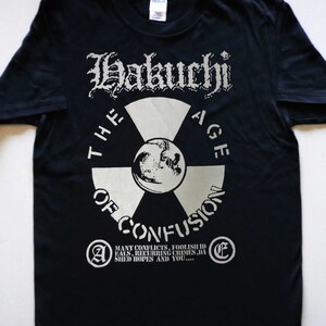 May include: Black t-shirt with a white graphic print of a stylized radiation symbol with the text "Hakuchi The Age Of Confusion" and a quote: "Many conflicts, foolish ideals, recurring crimes, dashed hopes and you..."
