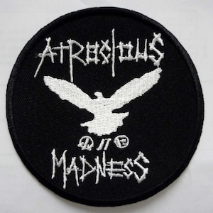 May include: A black and white embroidered patch with the text "Atrocious Madness" and a white dove with outstretched wings.