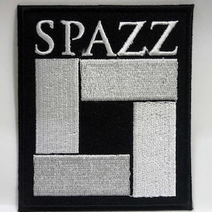 May include: A black and white embroidered patch with the word "SPAZZ" in white lettering and a white geometric design.