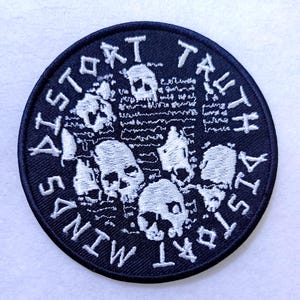 Könnte beinhalten: Schwarz-weiß gestickter Patch mit dem Text "Distort Trust Distort Minds" in einem kreisförmigen Design. Der Patch zeigt mehrere weiße Schädel auf schwarzem Hintergrund.