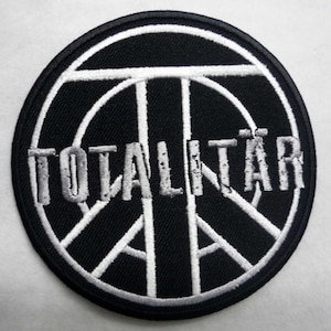 以下が含まれることがあります： 平和マークと白い文字で「TOTALITAR」と書かれた黒と白の刺繍パッチ