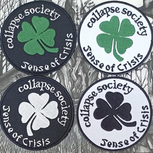 Peut inclure: Quatre patchs ronds brodés en noir et blanc avec un motif de trèfle et le texte "Collapse Society Sense of Crisis".