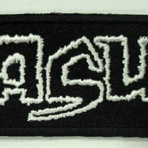 Peut inclure: Écusson en tissu noir avec du texte brodé blanc qui dit "NASUM".