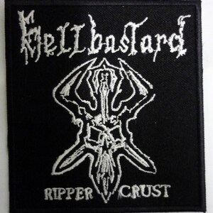 Könnte beinhalten: Schwarz-weiß gestickter Patch mit dem Text "Hellbastard" und "Ripper Crust" in einer gotischen Schriftart. Der Patch zeigt einen stilisierten Schädel mit Hörnern.