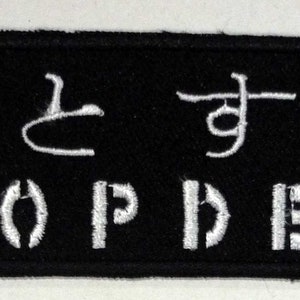May include: Black and white embroidered patch with the Japanese text "落として死" and the words "DROP DEAD" in white lettering.