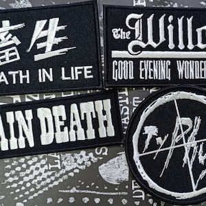 Könnte beinhalten: Vier schwarze gestickte Patches mit weißen Buchstaben. Die Patches zeigen den Text "畜生 DEATH IN LIFE", "The Willard GOOD EVENING WONDERFUL FIEND", "BRAIN DEATH" und ein stilisiertes Logo mit dem Text "TYRUS".
