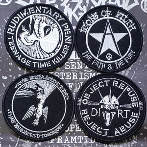 May include: Four black and white embroidered patches with circular borders. The patches feature various designs, including a skull, a star, a bird, and a lightning bolt. The text on the patches reads "Rudimentary Penny Killer", "Icons of Filth The Filth & The Fury", "You're Better Active Today Than Radioactive Tomorrow", and "Object Refuse Dirt Reject Abuse".