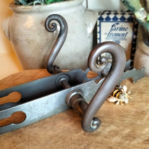May include: A pair of ornate black metal door handles with a decorative scroll design. The handles are attached to a metal plate with two keyholes.