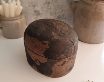 May include: A dark brown wooden hat box with a worn and weathered finish. The box is oval shaped and has a slight crack on the top.