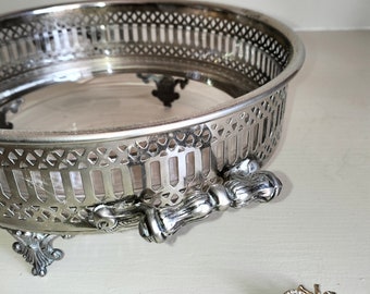 May include: A silver, decorative, footed bowl with a clear glass insert. The bowl has a delicate, openwork design and three ornate feet. A small, jeweled bee brooch is in the foreground.