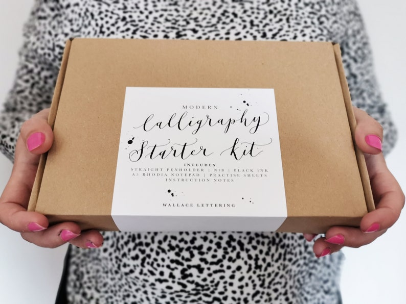 May include: A brown box with a white label that says "Modern Calligraphy Starter Kit" and lists the included items: straight penholder, nib, black ink, A5 Rhodia notepad, practice sheets, and instruction notes. The label also says "Wallace Lettering".