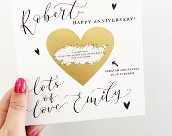 May include: A white card with a gold heart shape with a scratch-off area that says "Tim Minchin Songs the World Will Never Hear June 4th 7:30pm". The card says "Robert Happy Anniversary!" and "lots of love Emily" in black cursive writing.