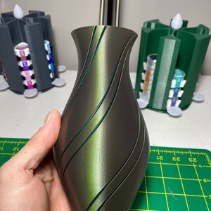 May include: A dark green and black vase with a swirling pattern. The vase is made of a smooth, glossy material.