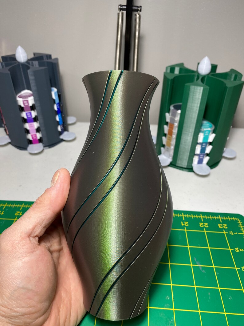 May include: A dark green and black vase with a swirling pattern. The vase is made of a smooth, glossy material.