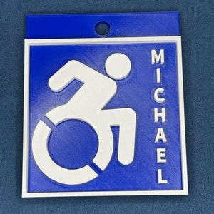 May include: Blue plastic keychain with a white accessibility symbol and the name "MICHAEL" printed vertically on the right side.
