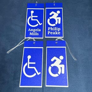 May include: Four blue luggage tags with white accessibility symbols and names. The tags are for Angela Mills, Philip Peake, and two others.