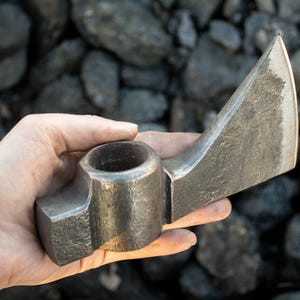 Pode incluir: Uma m&atilde;o segura um machado de estilo medieval com um cabo redondo e oco. A cabe&ccedil;a do machado &eacute; feita de metal e tem uma l&acirc;mina afiada.