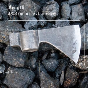 Pode incluir: Um machado de prata com cabo de madeira. O machado tem 15,5 cm de comprimento, 9 cm de largura e pesa 644 g. O machado est&aacute; sobre um leito de pedras pretas.