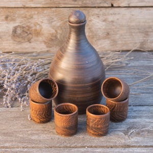 May include: A set of three ceramic mugs with a speckled, cream-colored glaze. Each mug features a different hand-painted design: a blue and green leaf, a yellow flower, and a red berry. The mugs have a simple, modern design.
