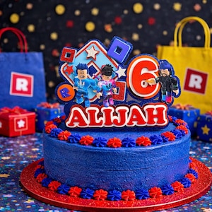May include: A blue birthday cake with red and blue frosting decorations. The cake is topped with a Roblox-themed cake topper with the name "Alljah" and the number "6". Blue gift bags and boxes are in the background.