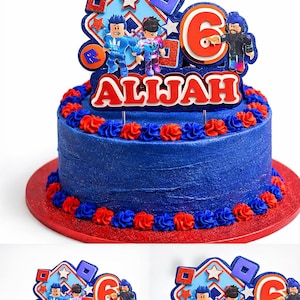 May include: A blue frosted birthday cake with red and blue frosting accents. The cake is decorated with a topper featuring cartoon characters, the number 6, and the name "ALLIJAH" in red. The cake sits on a red cake board.