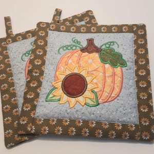 May include: Set of three brown and yellow quilted pot holders with a pumpkin and sunflower design.