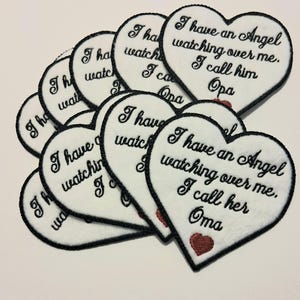 May include: A collection of heart-shaped patches with black stitched borders. The white patches feature the embroidered phrase "I have an Angel watching over me. I call him Opa" or "I call her Oma" in black script, with a small red heart.