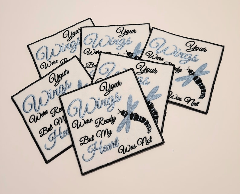 May include: A set of eight white fabric patches with black outlines and blue embroidery. Each patch features a dragonfly and the text "Your Wings Were Ready But My Heart Was Not".