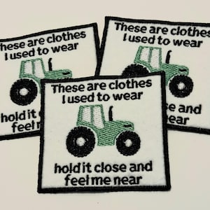 Puede incluir: Tres parches de tela blanca con contornos bordados en negro. Cada parche presenta un tractor verde con ruedas negras y el texto "These are clothes I used to wear" y "hold it close and feel me near".