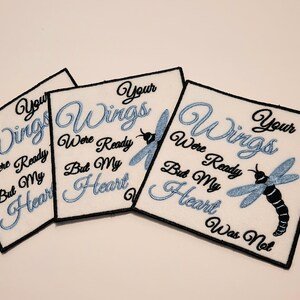 May include: Three white fabric patches with black embroidery. Each patch features a blue dragonfly and the text "Your Wings Were Ready But My Heart Was Not".