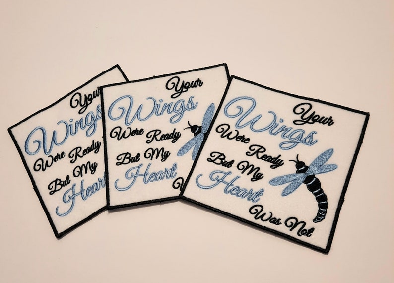 May include: Three white fabric patches with black embroidery. Each patch features a blue dragonfly and the text "Your Wings Were Ready But My Heart Was Not".