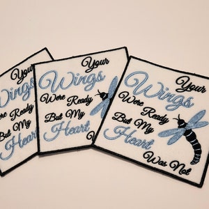 May include: Three white fabric patches with black embroidery. Each patch features a blue dragonfly and the text "Your Wings Were Ready But My Heart Was Not".