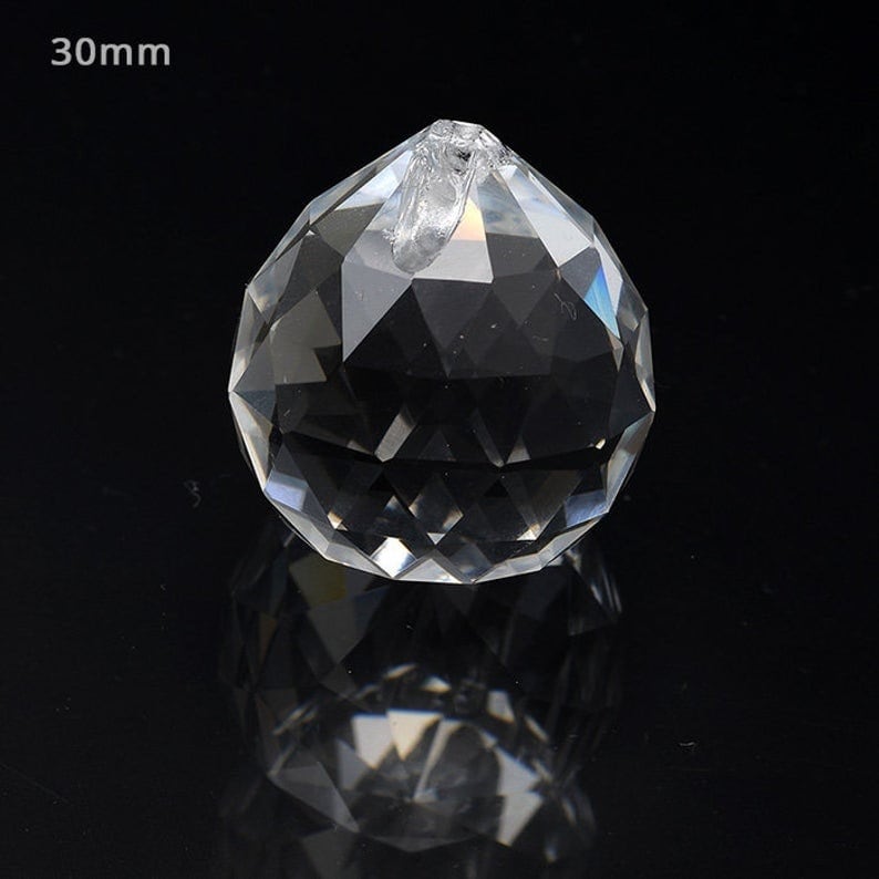 Peut inclure: Une boule de cristal transparente de 30 mm de diam&egrave;tre, avec un design facett&eacute;. La boule a une petite boucle en haut pour la suspendre.