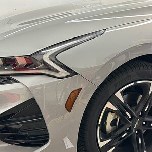 May include: A silver car with black wheels and a black front bumper. The car has a silver paint job and black accents. The headlights are on and the car is parked in a garage.