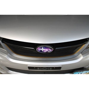 Könnte beinhalten: Ein silberner Subaru mit einem schwarzen Kühlergrill und einem Subaru-Logo im Galaxie-Design. Der Kühlergrill hat ein schwarzes Gittermuster und eine dünne goldene Einfassung.