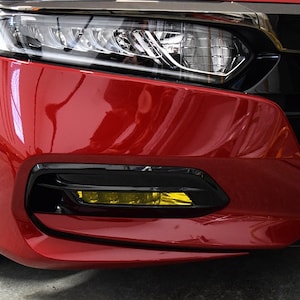 May include: A red car with yellow fog lights. The car has a black front bumper and a black grille.