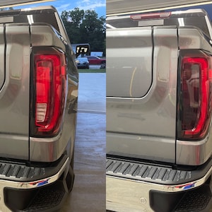 以下が含まれることがあります： グレーのピックアップトラックの後部をクローズアップした写真。テールライトが点灯しており、赤とクリアのレンズの組み合わせになっています。トラックにはクロームバンパーとブラックテールゲートが付いています。