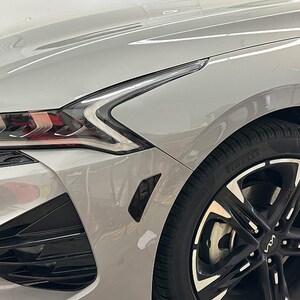 May include: A silver car with black wheels and a black front bumper. The car has a black grill and black headlights. The car is parked in a garage.