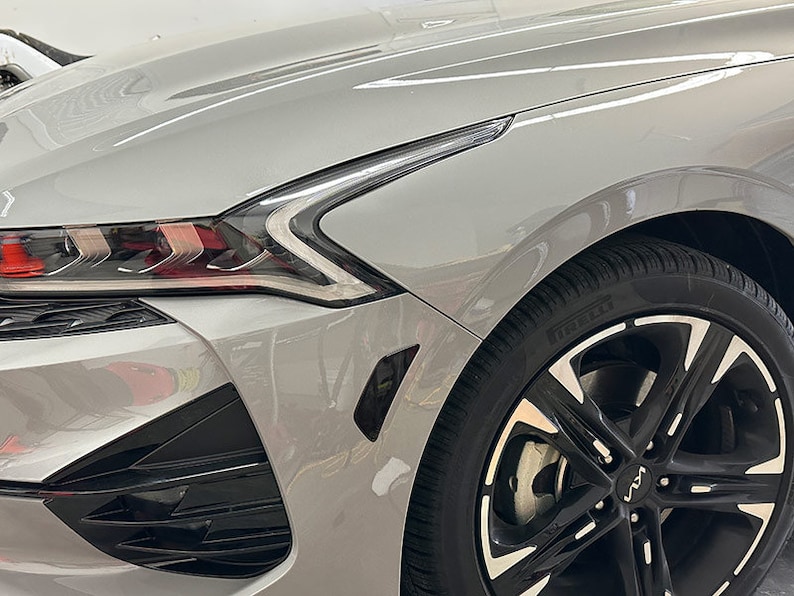 May include: A silver car with black wheels and a black front bumper. The car has a black grill and black headlights. The car is parked in a garage.