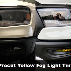 May include: A white pickup truck with a pre-cut yellow fog light tint. The tint is applied to the fog lights, giving them a yellow hue. The truck is parked on a driveway.