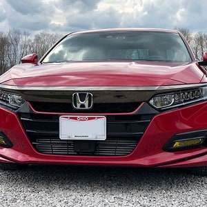 Op de afbeelding: Een rode Honda Accord sedan met een zwarte grille en koplampen. De auto heeft een zwart kenteken met het woord "OHIO" erop. De auto staat geparkeerd op een grindpad.